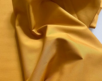 May include: A close-up of a smooth, golden yellow fabric. The fabric is folded and draped, showing its texture and color.