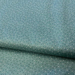 Puede incluir: Una tela de color verde azulado con un patrón de lunares blancos. La tela tiene una textura sutil y está doblada por la mitad.