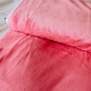 May include: A close-up of a soft, pink and red plush fabric. The fabric is folded in half, with the pink side on top and the red side on the bottom.