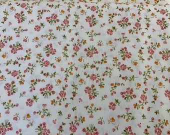 May include: White fabric with a small-scale floral print. The flowers are pink and the stems are green. There are also small orange dots scattered throughout the fabric.