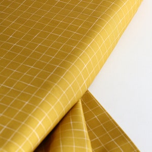May include: A yellow fabric with a white grid pattern. The fabric is folded in half and the edges are visible.