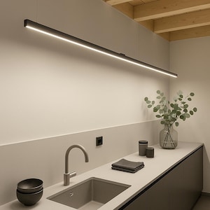 Peut inclure: Intérieur de cuisine moderne avec un long luminaire LED linéaire noir suspendu au-dessus d'un comptoir. Le comptoir comprend un évier gris, un robinet et un vase avec de la verdure. Des meubles bas gris foncé et un plafond en bois complètent le design.