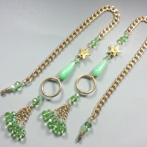 May include: A pair of gold chain earrings with green glass beads and gold star charms. The earrings have a tassel of green glass beads at the bottom.