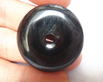 Könnte beinhalten: Eine schwarze, runde, donutförmige Perle mit einem Loch in der Mitte. Die Perle hat eine glatte, polierte Oberfläche.