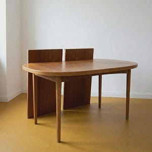 Könnte beinhalten: Ein hölzerner Esstisch mit einer glatten, ovalen Tischplatte und vier konisch zulaufenden Beinen. Der Tisch verfügt über zwei vertikale Holzpaneele, die aufrecht an der Rückseite angebracht sind und eine markante Struktur bilden.