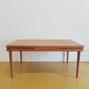 May include: A rectangular wooden coffee table with a light brown finish. The table has four tapered legs and a recessed area on the sides. The table is approximately 122 cm long and 61 cm wide.