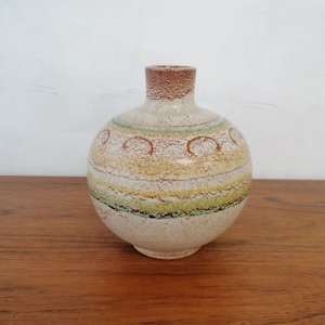 Può includere: Un vaso in ceramica bianca con corpo rotondo e collo stretto. Il vaso ha un bordo marrone ed è decorato con strisce marroni, gialle e verdi e una glassa craquelé.