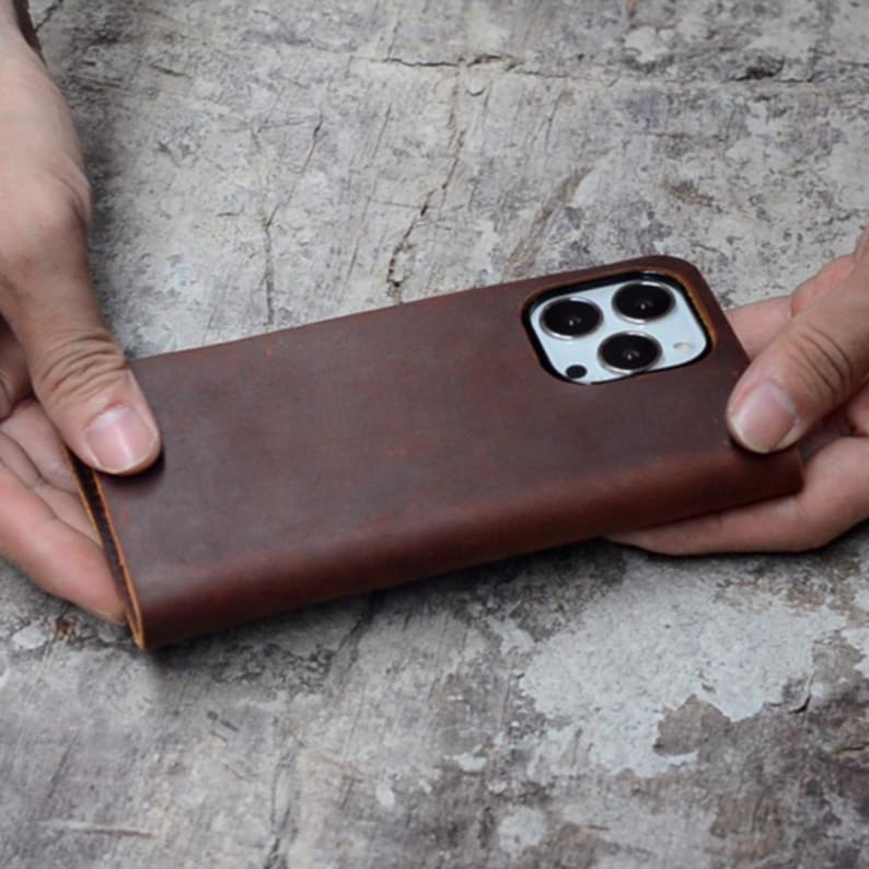 May include: A brown leather phone case with a cutout for the camera lens.