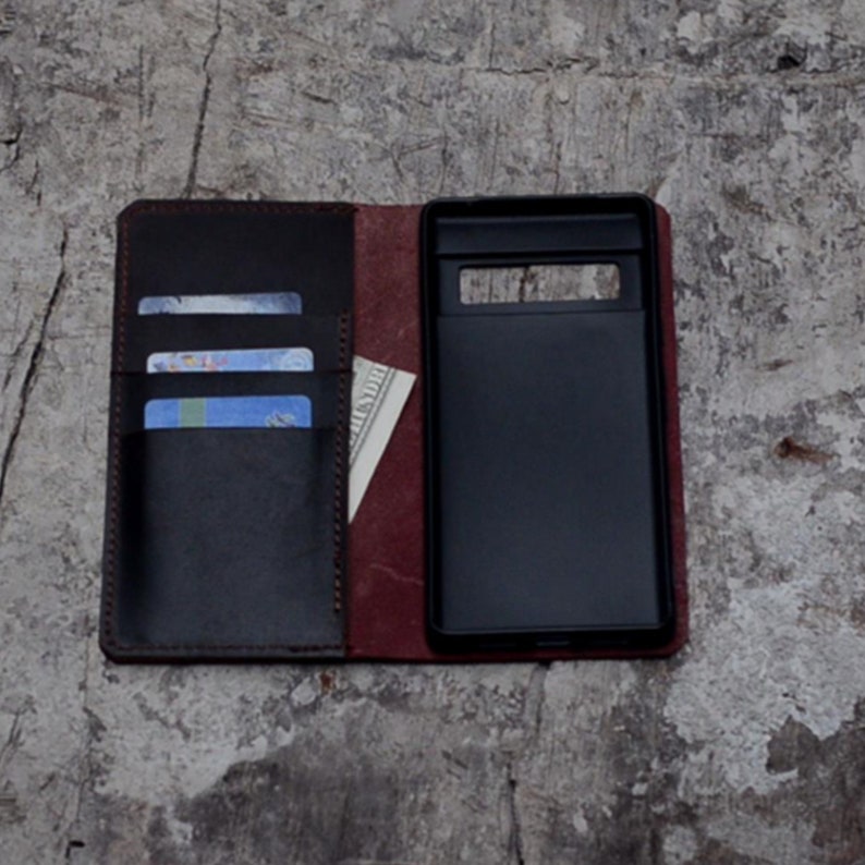 May include: A brown leather phone case with a flap that opens to reveal slots for credit cards and cash. The case has a black phone holder with a cutout for the camera.