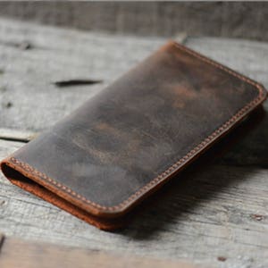 May include: A brown leather wallet with a distressed finish and a stitched edge.