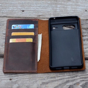 May include: A brown leather phone case with a flap that opens to reveal a phone slot and card slots. The case is open and shows a black phone inside.