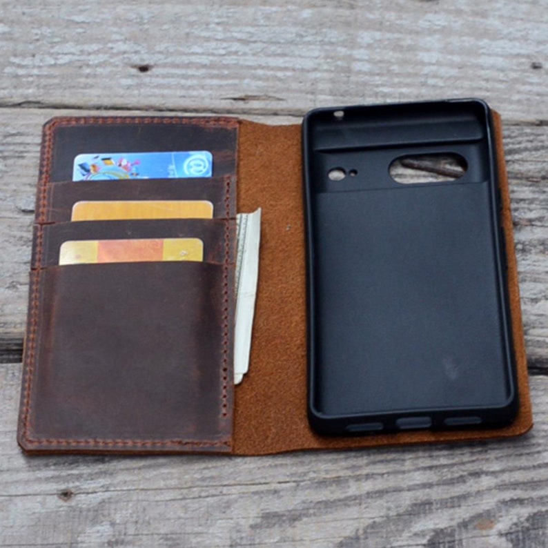 May include: A brown leather phone case with a flap that opens to reveal a phone slot and card slots. The case is open and shows a black phone inside.