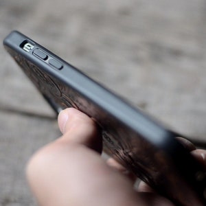 May include: A black phone case with a textured design. The case has a volume button and a power button on the side.
