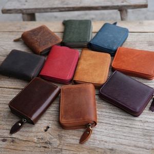 Op de afbeelding: Een verzameling portemonnees met ritssluiting in verschillende kleuren, waaronder bruin, rood, groen en blauw. De portemonnees zijn gemaakt van leer en hebben een rechthoekige vorm met een ritssluiting. De portemonnees zijn gerangschikt op een houten oppervlak.