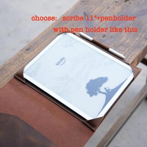May include: A brown leather Kindle Scribe 11" case with a pen holder. The Kindle is white with a tree graphic and the Amazon Kindle logo. A brown and white stylus rests on the screen. Text in the image reads: "choose: scribe 11"+penholder with pen holder like this."