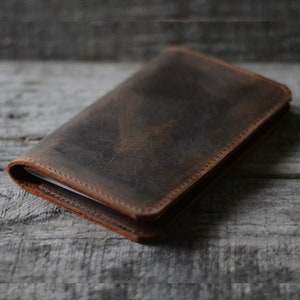 May include: A brown leather notebook with a distressed finish. The notebook has a stitched edge and is closed.