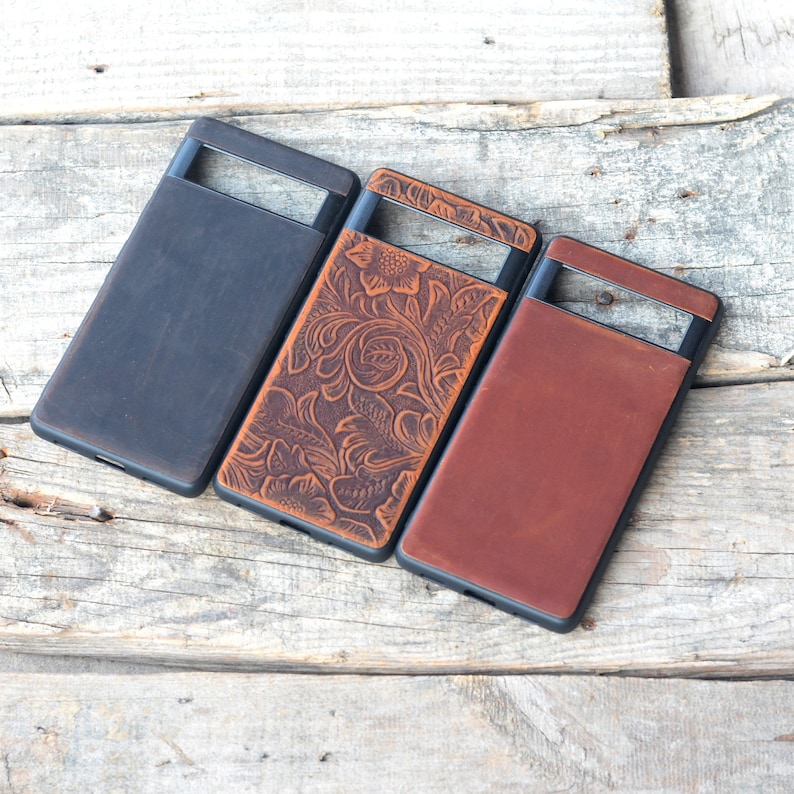 Puede incluir: Tres fundas para tel&eacute;fono hechas de cuero. Las fundas son de color marr&oacute;n, negro y marr&oacute;n con un patr&oacute;n floral. Las fundas tienen un recorte para el objetivo de la c&aacute;mara.