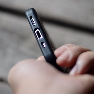 May include: A black phone case with a textured surface and a cutout for the charging port.