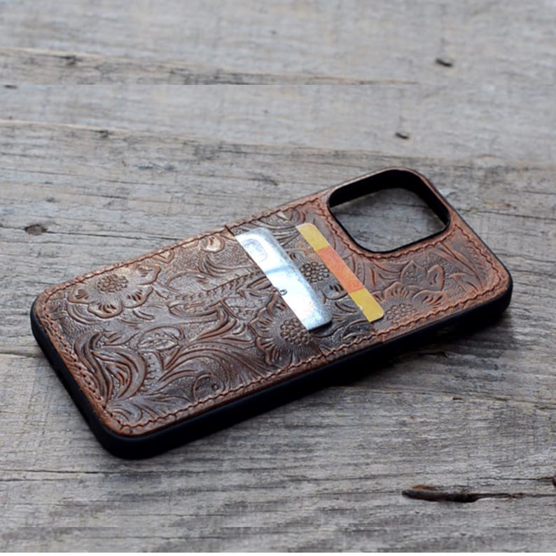 May include: A brown leather phone case with a floral embossed design. The case has a built-in card holder with a credit card visible.