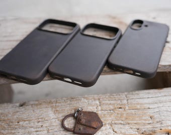 May include: Three dark gray phone cases and a small, rusty metal padlock rest on a weathered wooden surface. The phone cases are rectangular with openings for the camera and buttons. The padlock is detailed with rivets.
