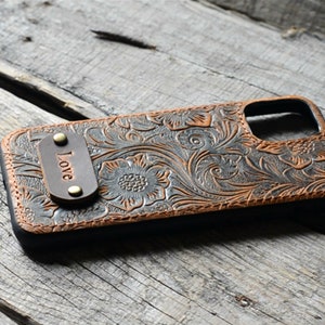 Peut inclure: Une coque de t&eacute;l&eacute;phone en cuir marron avec un motif floral et un petit patch en cuir qui dit "Love".