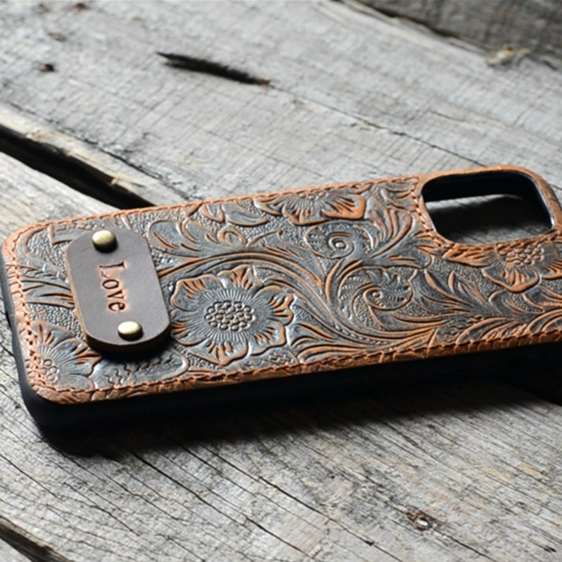 Peut inclure: Une coque de t&eacute;l&eacute;phone en cuir marron avec un motif floral et un petit patch en cuir qui dit "Love".