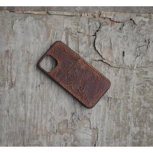 Puede incluir: Una funda de teléfono de cuero marrón con un diseño floral en relieve y una ranura para tarjeta.