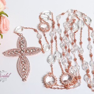 May include: Rose gold and clear crystal rosary with a large rose gold cross encrusted with rhinestones. The rosary is on a white background.