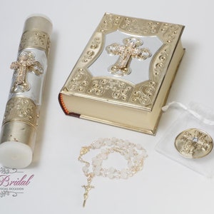 May include: A set of gold and silver religious baptism gifts including a candle, a rosary, a book, and a small pouch with a medallion.