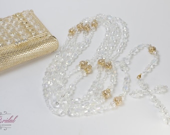 Puede incluir: Una caja de metal dorado con cuentas de cristal transparente y una larga hebra de cuentas de cristal transparente con detalles dorados. Las cuentas están enhebradas en un patrón.