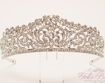Könnte beinhalten: Silberne Tiara mit einem zarten floralen Design und klaren Strasssteinen. Die Tiara befindet sich auf einem weißen Hintergrund.