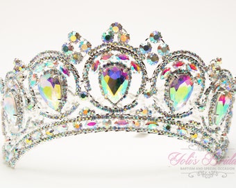 May include: A silver tiara with iridescent rhinestones. The tiara has a pointed crown and a curved base.