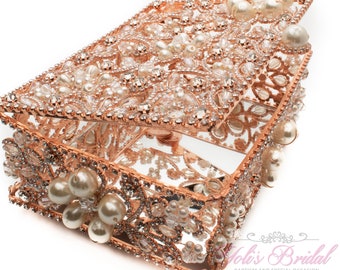 May include: Rose gold rectangular jewelry box with an open lid. The box is adorned with pearls and clear crystals. The interior of the box has a mirrored surface. The box is decorated with floral and leaf patterns.