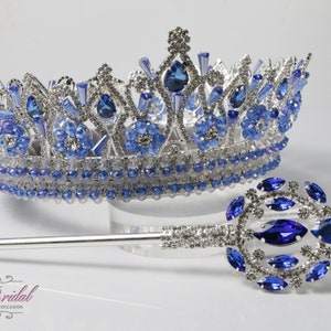 Op de afbeelding: Een zilveren en blauwe bruidskroon en scepter set. De kroon heeft een gedetailleerd ontwerp met blauwe en heldere kristallen. De scepter heeft een bijpassend blauw kristallen ontwerp. De set wordt op een witte achtergrond weergegeven.