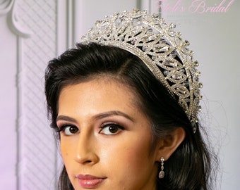 May include: A woman wearing a silver tiara with rhinestones and a dark blue dress with lace detailing.  She is wearing silver earrings.
