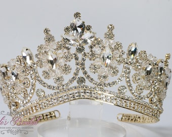 Puede incluir: Una corona dorada con adornos de cristal transparente. La corona tiene un delicado diseño floral y está adornada con brillantes pedrería.