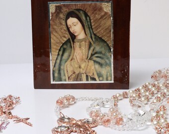 Puede incluir: Un conjunto de dos rosarios con acabado en oro rosa. Los rosarios están hechos con cuentas transparentes y blancas y presentan una gran cruz de oro rosa con cristales transparentes. También se incluye una caja de madera con una imagen de la Virgen María.