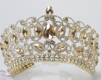 Puede incluir: Una corona dorada con diamantes de imitación transparentes y ámbar. La corona tiene un diseño delicado y ornamentado y es perfecta para una ocasión especial.