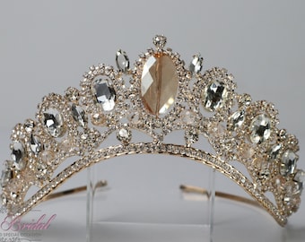 Puede incluir: Una tiara dorada con diamantes de imitación transparentes y ámbar. La tiara tiene un diseño delicado con una forma curva.