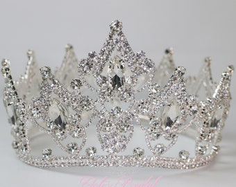May include: A silver crown with clear rhinestones. The crown has a pointed top and a circular base.