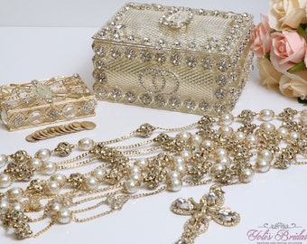 May include: A gold and white pearl rosary with a gold cross and crystal accents. The rosary is displayed with two gold boxes decorated with rhinestones and a bouquet of pink roses.