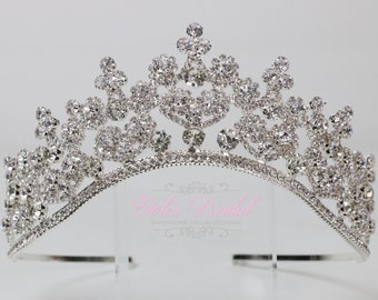 Könnte beinhalten: Eine silberne Tiara mit einem zarten Design und klaren Strasssteinen. Die Tiara ist gebogen und hat ein schlichtes Band.