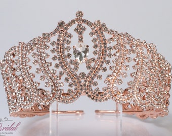Puede incluir: Tiara de oro rosa con diamantes de imitación transparentes y un gran cristal transparente en el centro. La tiara tiene un diseño delicado e intrincado.