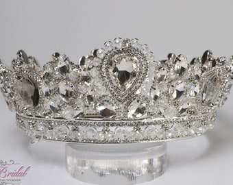 May include: Silver crown with clear rhinestones and a large clear crystal in the center. The crown is on a clear stand.