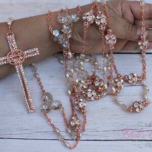 Può includere: Rosario in oro rosa con perline di cristallo e una grande croce in oro rosa con strass.