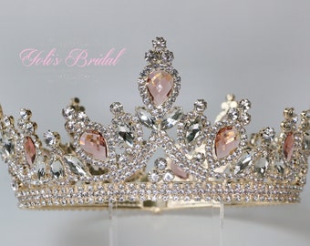 May include: A gold crown with clear and pink rhinestones. The crown has a pointed top and a rounded base.