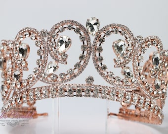 Puede incluir: Corona de oro rosa con diamantes de imitación transparentes. La corona tiene un diseño delicado e intrincado con espirales y piedras en forma de lágrima.