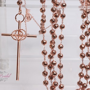 Può includere: Collana di rosario in oro rosa con un ciondolo a croce abbinato. Le perle sono rotonde e hanno una superficie testurizzata. La croce ha un design a doppio cerchio.