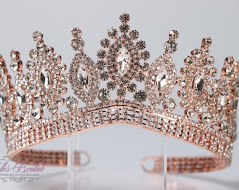Puede incluir: Corona de oro rosa con diamantes de imitación transparentes. La corona tiene una parte superior puntiaguda y una base ancha.