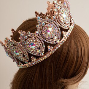 May include: A rose gold crown with iridescent rhinestones. The crown has a pointed top and a circular base.